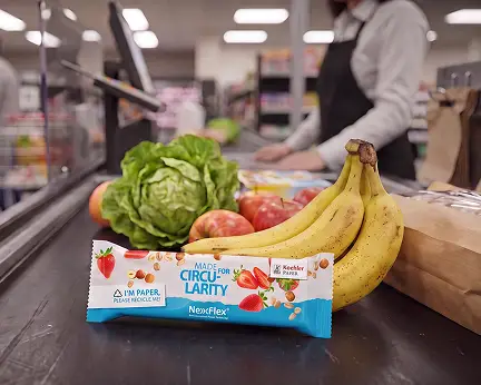 Snack bar in recyclable wrapper with "Made for Circularity" claim at supermarket checkout, next to bananas, lettuce and apples.