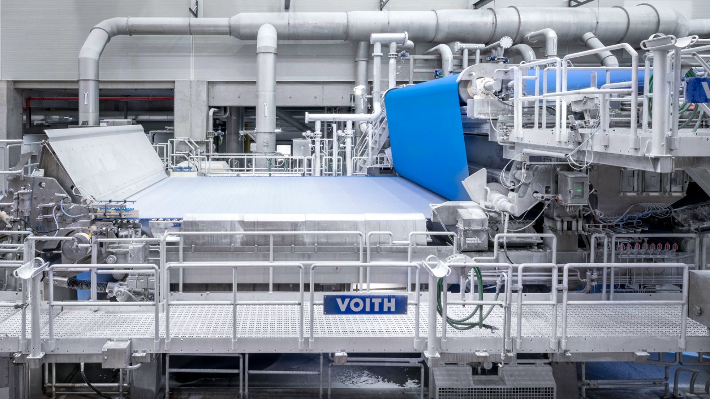 Modern paper machine system with wide production web and distinctive blue belt section in a bright industrial setting