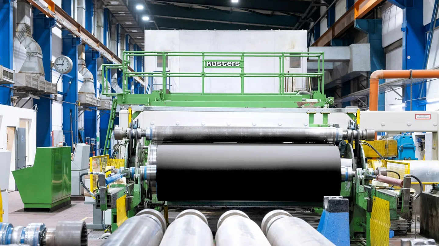 Industrial paper machine setup with large rollers inside a spacious manufacturing hall