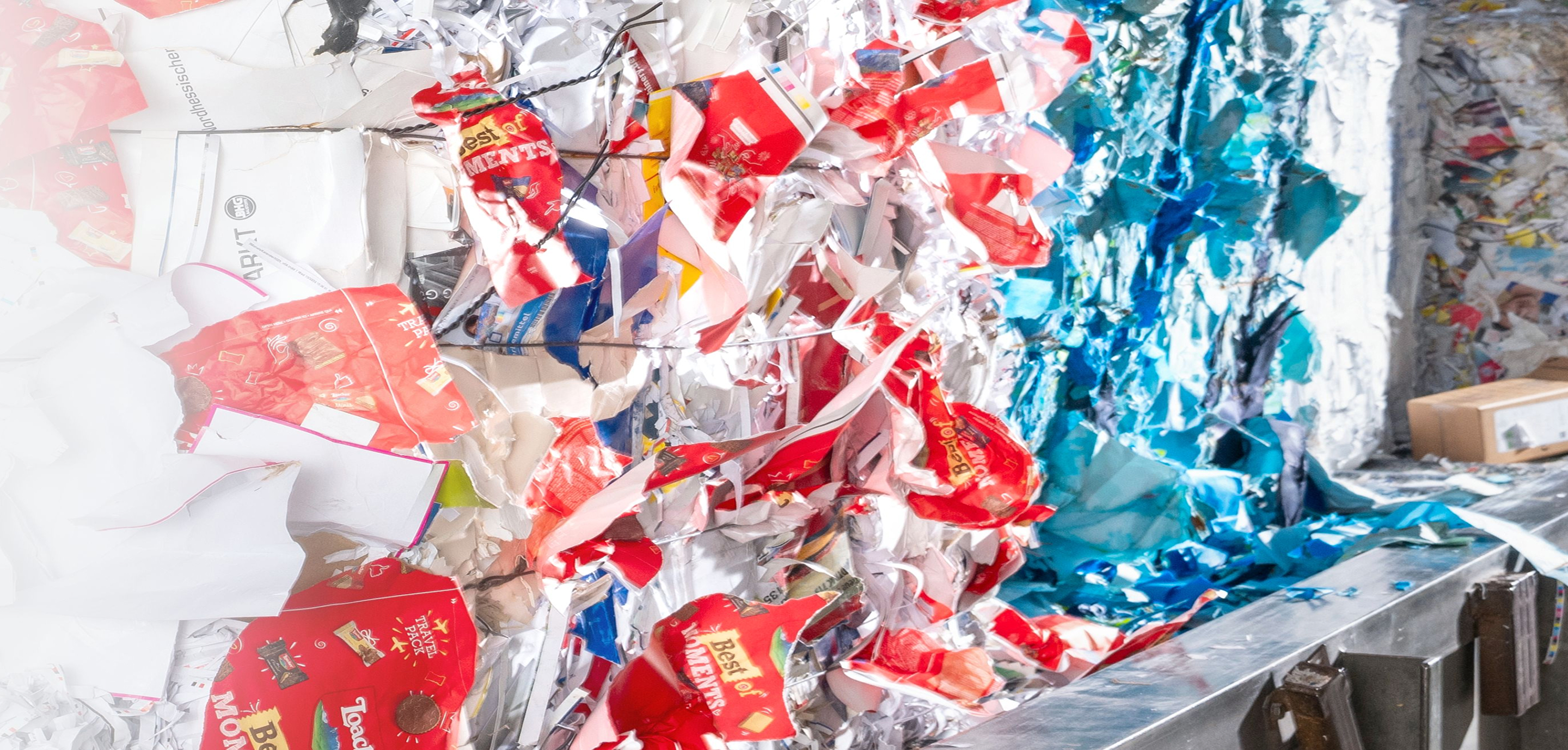 Compressed bales of colorful recycled packaging scraps in red, blue and white tones inside a waste sorting facility