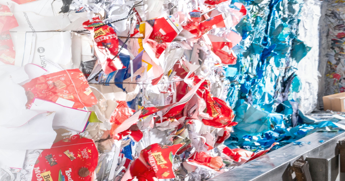 Compressed bales of colorful recycled packaging scraps in red, blue and white tones inside a waste sorting facility