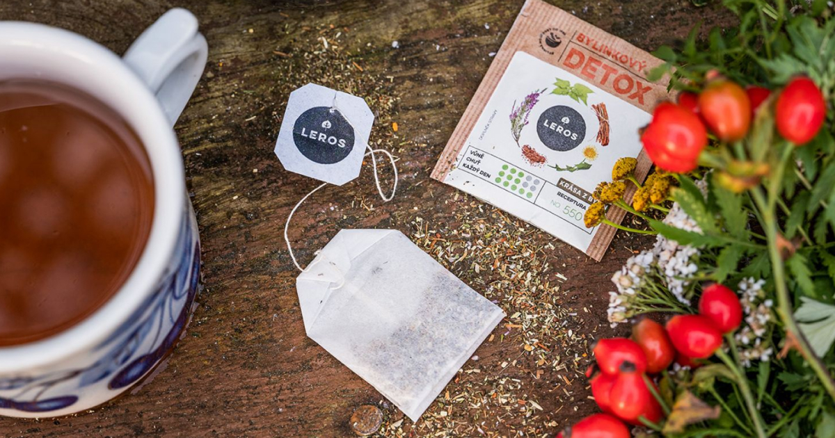 Cup of herbal tea with LEROS teabag, detox sachet and fresh red berries and herbs arranged on a rustic wooden surface