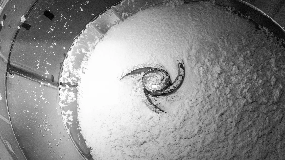Circular metal mixer with spiral blades churns bright white paper pulp, close-up view of industrial production step