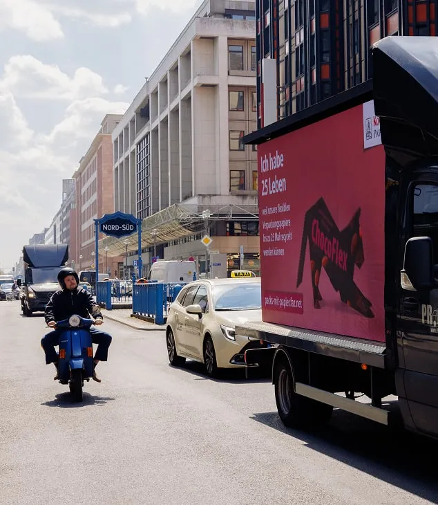 Advertising truck with  "Pack's mit Papier" screen and "Ich habe 25 Leben" slogan drives through Berlin government district past scooter