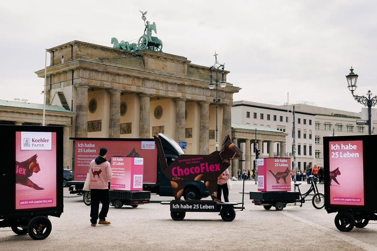 Brandenburg Gate with pink Koehler Paper vehicles for "Pack's mit Papier" campaign, screens with "Ich habe 25 Leben" slogans